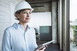 © Westend61 - Thoughtful engineer wearing hardhat standing with tablet PC in office