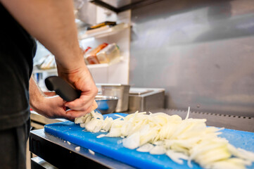 Wall Mural - A close-up of hands slicing onions on a blue cutting board, with kitchen utensils in the background. Perfect for culinary, cooking, and kitchen-related themes. High-resolution, well-lit, and detailed.