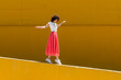 © VISTA by Westend61 - Woman with arms outstretched walking on yellow wall