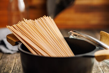 Wall Mural - Uncooked whole grain pasta. Raw spaghetti in black pot.