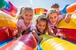 © Alex - Smiling children enjoying a sunny day playing on a colorful inflatable slide at an outdoor event.
