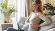 © SHI - Woman suffering from back pain while working on laptop at home on sofa