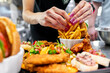 © pavel siamionov - Close-up of hands with purple nails serving French fries in a fast-food restaurant. Blurred burgers and fried chicken in the background.