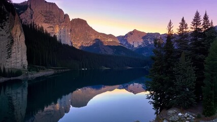 Wall Mural - Rugged cliffs and towering pine trees frame the peaceful mountain lake as the soft light of dusk begins to illuminate the scene.