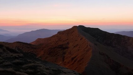 Sticker - As the sky slowly changes from dark blue to shades of soft pink and orange the mountainside is bathed in a warm golden light.