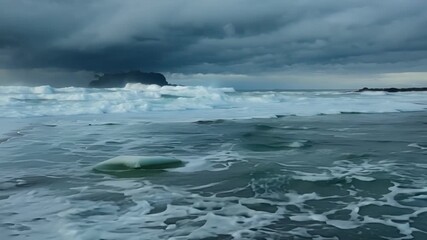 Wall Mural - The icy waves stand in stark contrast to the dark stormy skies above creating a striking image of natures power.