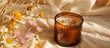 © StockKing - Handmade soy wax candle in an amber glass adorned with dried flowers, set against a beige background, featuring copy space image.