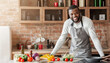 © Prostock-studio - Attractive black positive man posing at kitchen while cooking dinner for his family, free space