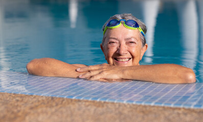 Sticker - Happy active senior woman doing sport in the outdoor swimming pool looks at camera smiling. Elderly woman and healthy lifestyle in retirement or vacation