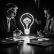 © Preeyanuch - Two professionals strategizing in a dark room, illuminated by a glowing light bulb, symbolizing innovation and brainstorming.