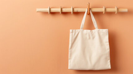 Stylish canvas tote bag hanging on a wooden rack against a warm, peach-colored wall, ideal for eco-friendly shopping.