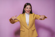 © amnaj - Smiling businesswoman wearing a yellow blazer pointing both her index fingers to the sides on a purple background