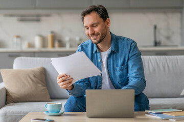 Poster - A man in a blue shirt sits on a couch, reviewing documents while working on his laptop. A cup of coffee sits on a table in front of him, alongside a phone and notebooks.
