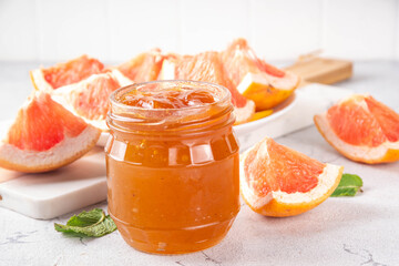 Homemade grapefruit jam, sweet pink grapefruit marmalade in small jar, with grapefruit slices and mint leaves on white table background