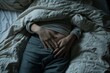 © Xyeppup - A person lying in bed under a white blanket, with their hands resting on their abdomen, suggesting discomfort or pain