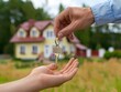 © ParinApril - A hand transfers a house key to another hand, symbolizing home ownership and new beginnings in front of a colorful house.