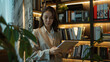 © Jirawatfoto - Professional woman with a tablet in a contemporary library, standing among books and green plants.