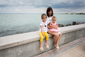 Mother with two young daughters sitting by the sea on a cloudy day