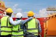© Stella - Group of engineer workers with safety vest and helmet from behind hugging friend neck while standing at construction building site. Architect team working together at building site workplace.