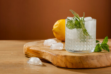 Wall Mural - Cold brew water drink with ice cubes and fresh rosemary and mint leaves. Yellow lemons and copy space on wooden table. 