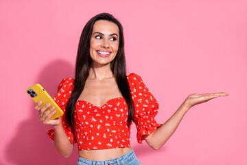 Wall Mural - Photo of brunette hispanic young lady in bright red blouse using smartphone demonstrate online products isolated on pink color background