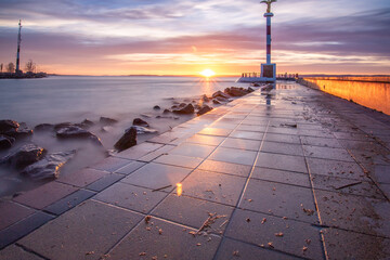 Wall Mural - a small marina on a lake. Breakwater and pillar with golden figure in the dreamy sunset. Landscape shot in Siófok, Balaton, Hungary