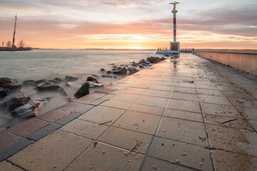 Wall Mural - a small marina on a lake. Breakwater and pillar with golden figure in the dreamy sunset. Landscape shot in Siófok, Balaton, Hungary