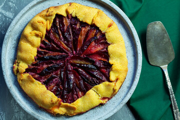 Traditional french pie galette made of corn dough with plum filling on a concrete tray.