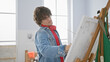 © Krakenimages.com - Handsome young man with curly hair painting on an easel in a bright art studio, exuding creativity and concentration.