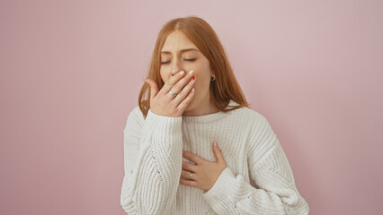 Wall Mural - A young caucasian woman in a white sweater is yawning against an isolated pink background.