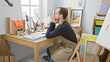 © Krakenimages.com - Pensive bearded man in apron sitting at a desk filled with artistic supplies in a well-lit studio