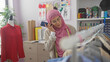 © Krakenimages.com - A young woman in a hijab converses on the phone inside a busy tailor shop filled with colorful threads, fabric, and garments.