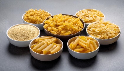 Wall Mural - different shapes of dried pasta like elbow macaroni and bowtie pasta are displayed in bowls on a grey surface along with couscous and other pasta varieties