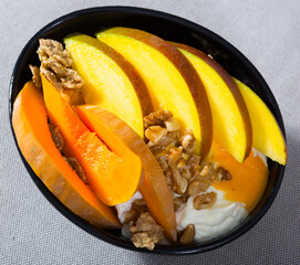 Wall Mural - Pumpkin slices bake in the oven, cut the mango. Oat flakes, whipped cream, dried fruits on a plate with pumpkin and mango