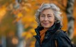 © imagineRbc - A joyful senior woman strolls through a vibrant autumn park, smiling as she enjoys the beautiful fall foliage surrounding her