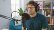 © Krakenimages.com - Concentrated hispanic man recording in a well-equipped podcast studio, wearing headphones and speaking into a microphone.