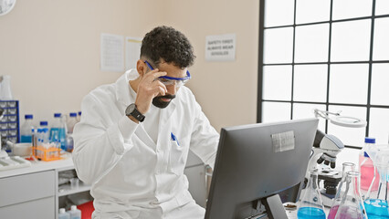 Sticker - Bearded man analyzes data on computer in a modern laboratory setting with microscope and glassware present.