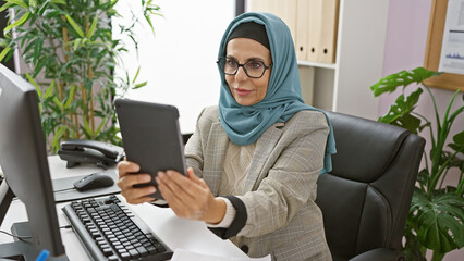 Wall Mural - Professional woman in hijab using tablet in modern office, conveying diversity and technology in the workplace.