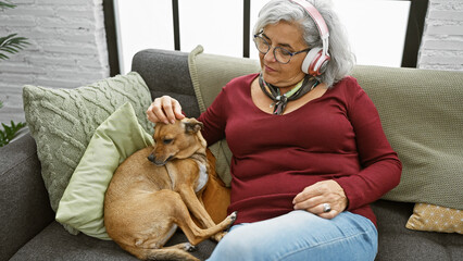 Poster - A mature woman with grey hair listens to music while petting her dog on a cozy sofa indoors