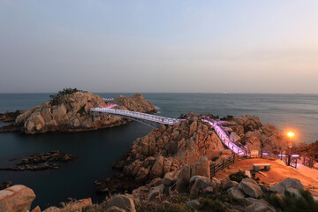 Wall Mural - Daewangam Park, Dong-gu, Ulsan, South Korea - December 13, 2022: Sunset and night view of trail and bridge on the sea connecting Daewangam Rock with pink illumination
