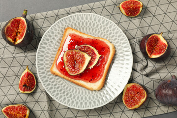 Figs, piece of bread with jam on plate on gray background, top view