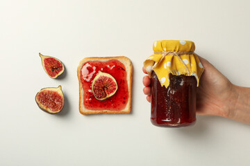 Sticker - Figs, jar of jam in hand and piece of bread on white background, top view