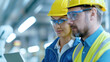 © TH_Stock - Male and female engineer in yellow hard hats and safety glasses closely analyze data on a laptop in an industrial setting, with modern machinery in the background, emphasizing precision and teamwork.
