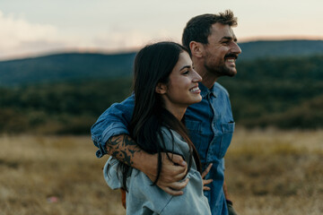 Loving couple embracing and following the trail along a grassy mountain ridge and having fun together. Healthy lifestyle and romantic getaway