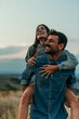 © La Famiglia - Couple having a piggyback ride, happy and smile hug in nature on a travel, adventure and road trip outdoor