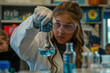 © Sady - A young, enthusiastic female scientist wearing safety goggles and a white lab coat is conducting a chemistry experiment in a well-equipped high school laboratory. She is carefully pouring a vibrant bl