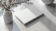 © LittleDreamStocks - Blank white booklet mockup on a table with a vase of flowers.