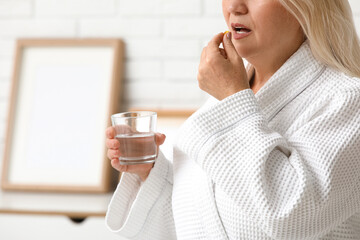 Wall Mural - Beautiful mature woman with glass of water taking pill at home