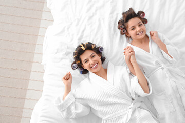 Poster - Little girl and her mother with hair curlers lying on bed, top view