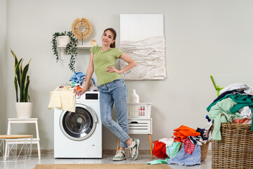 Wall Mural - Young woman with dirty laundry on washing machine at home